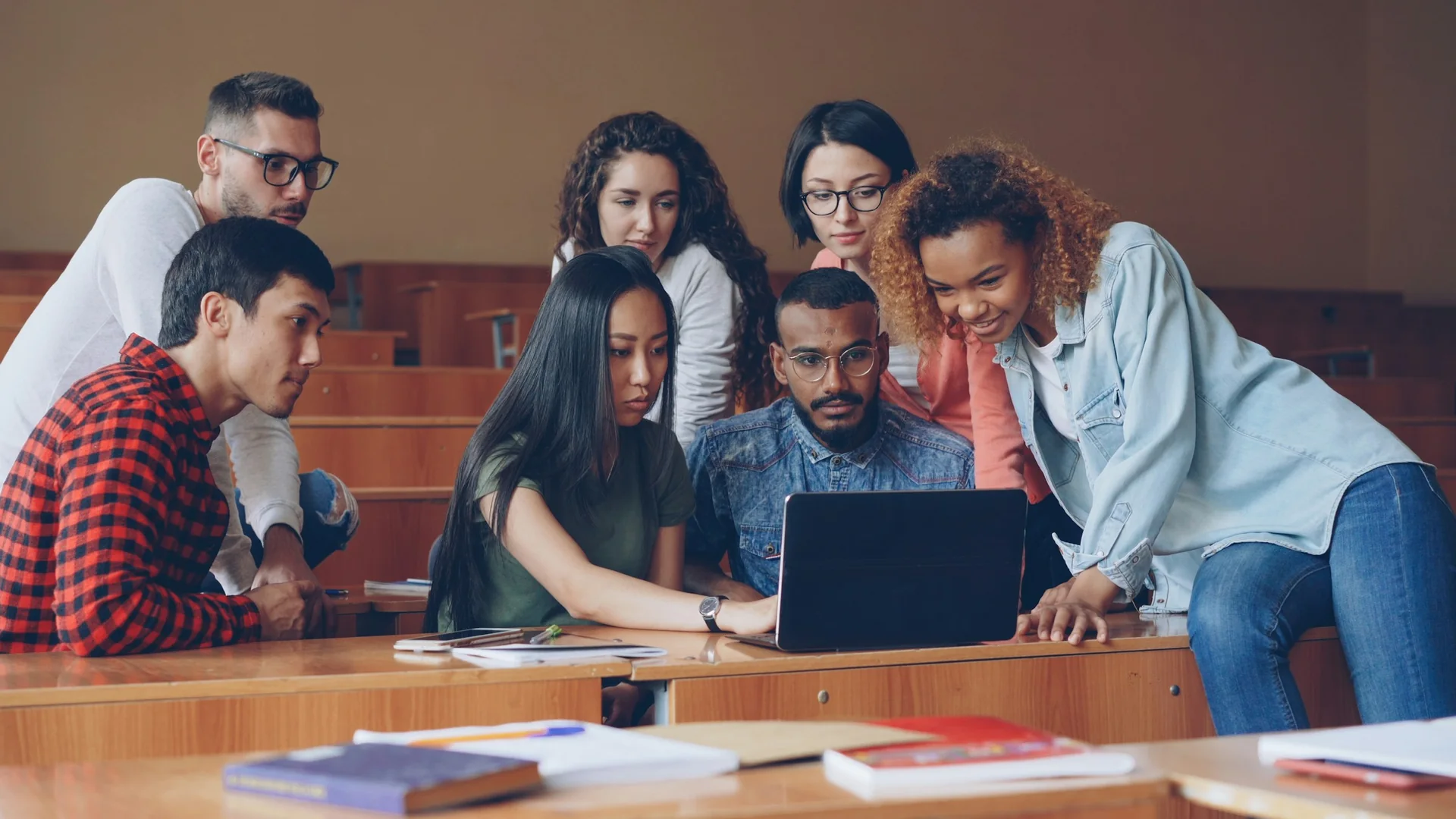 A diverse group of adults learning together around a laptop